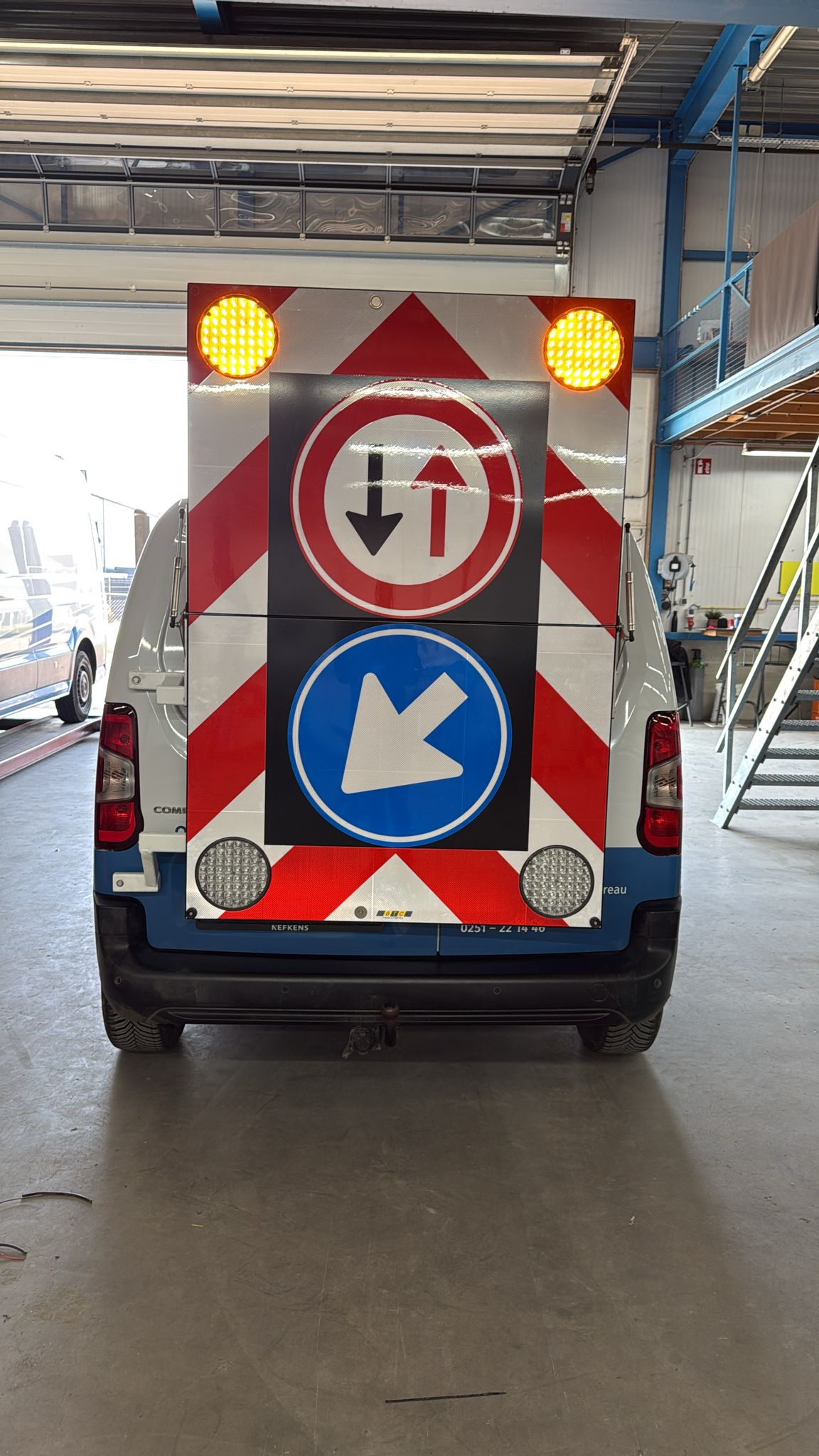 BTC actieraam op bedrijfsbusje in de werkplaats — bord met inhaalverbod en blauw richtingbord, gele LED-verlichting